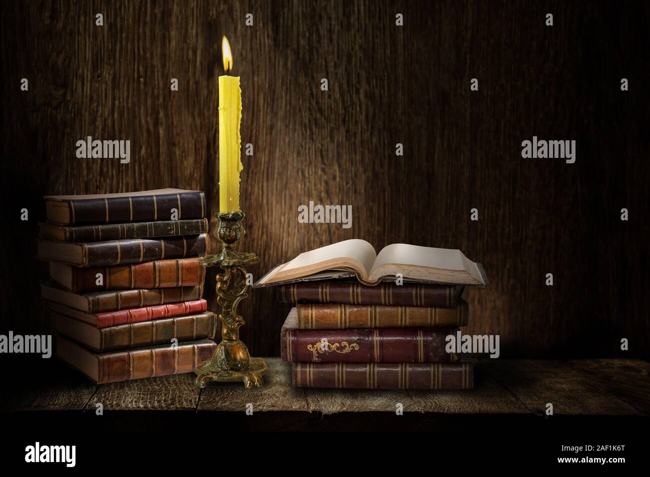 Candélabre rétro avec des bougies allumées et des livres sur fond sombre en bois Banque D'Images