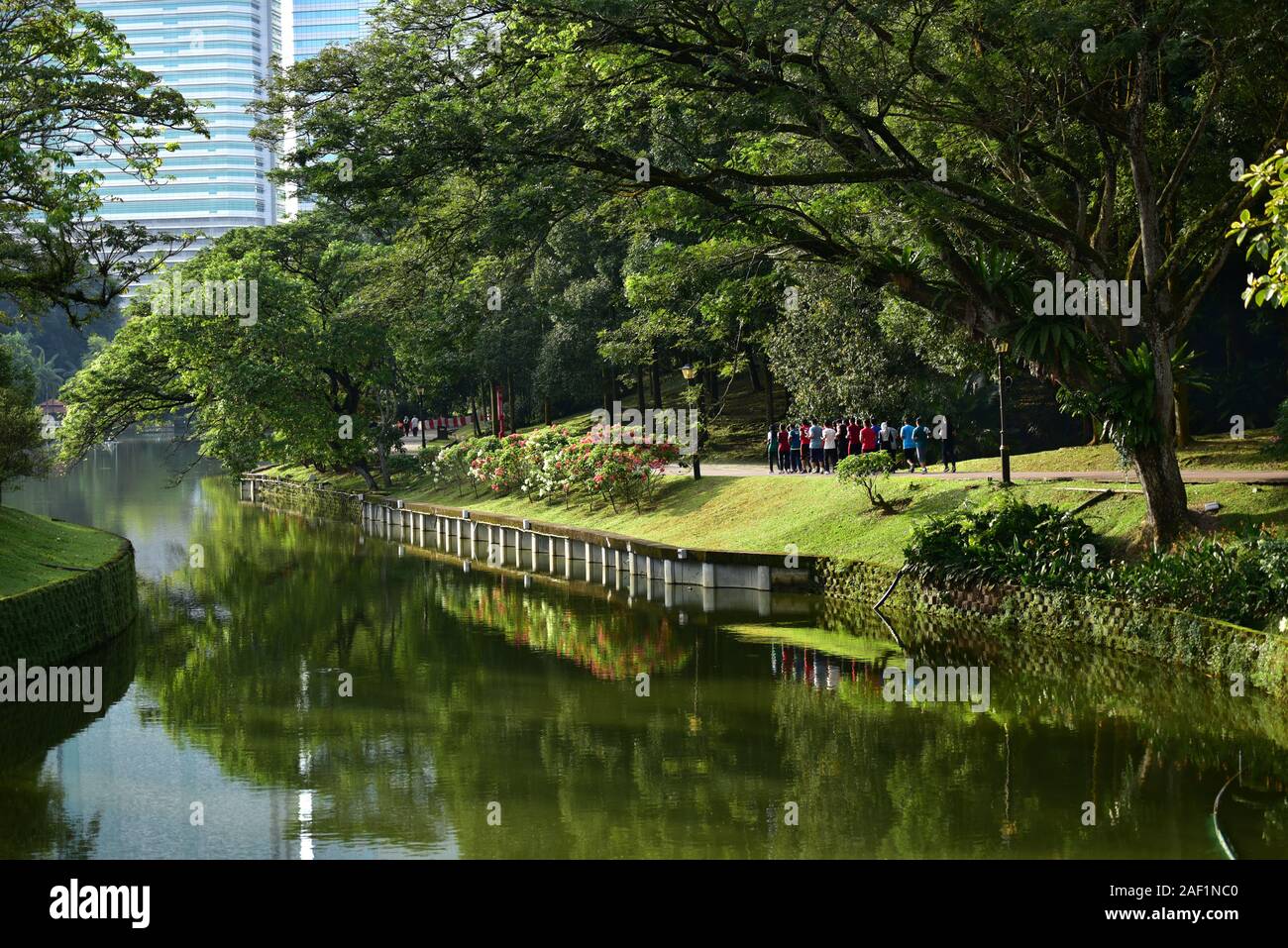 Groupe de personnes exécutant au jardin botanique avec des gratte-ciel en arrière-plan. Kuala Lumpur Banque D'Images