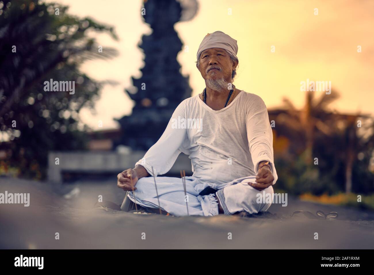 Bali, Indonésie - 10 déc 2019 : old man balinais locales dans la méditation près de la mer. Concept de prier. La pratique du yoga adultes sur la plage de sable noir de Keramas Banque D'Images