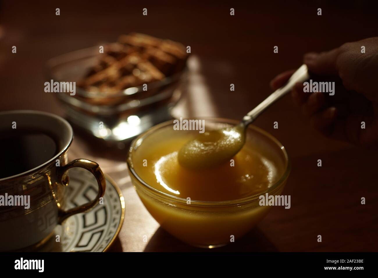 L'heure du thé. Le miel dans un bol en verre avec une cuillère, une tasse de thé sur la soucoupe, les cookies dans un vase sur la table. Banque D'Images