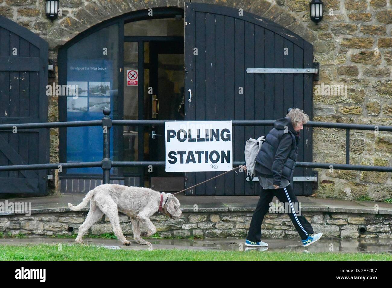 West Bay, Dorset, UK. 12 décembre 2019. Femme avec un chien passe devant le bureau de vote à la maison de sel de West Bay, dans le Dorset le jour de l'élection générale. Crédit photo : Graham Hunt/Alamy Live News Banque D'Images