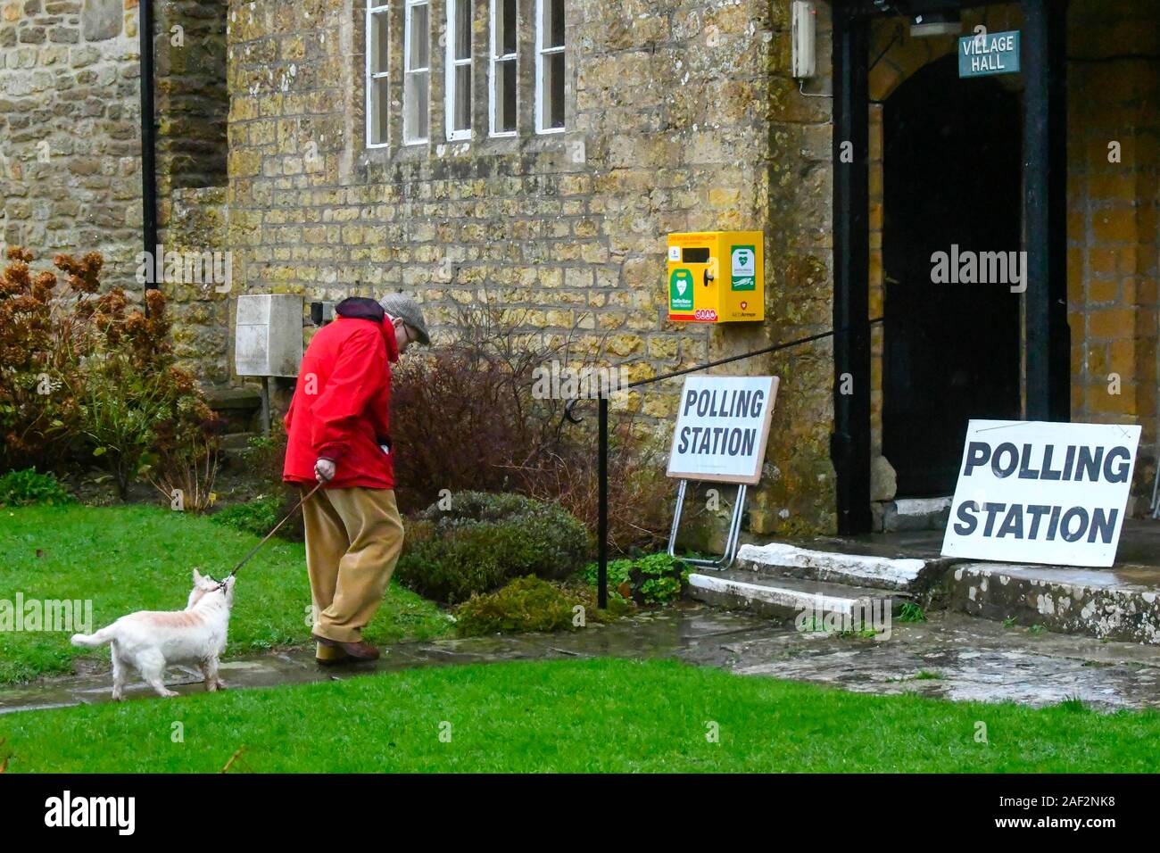 Walditch, Dorset, UK. 12 décembre 2019. Un homme portant une veste imperméable arrivant avec son chien sous la pluie pour voter au bureau de vote à Walditch dans Dorset sur un jour de l'élection générale. Crédit photo : Graham Hunt/Alamy Live News Banque D'Images