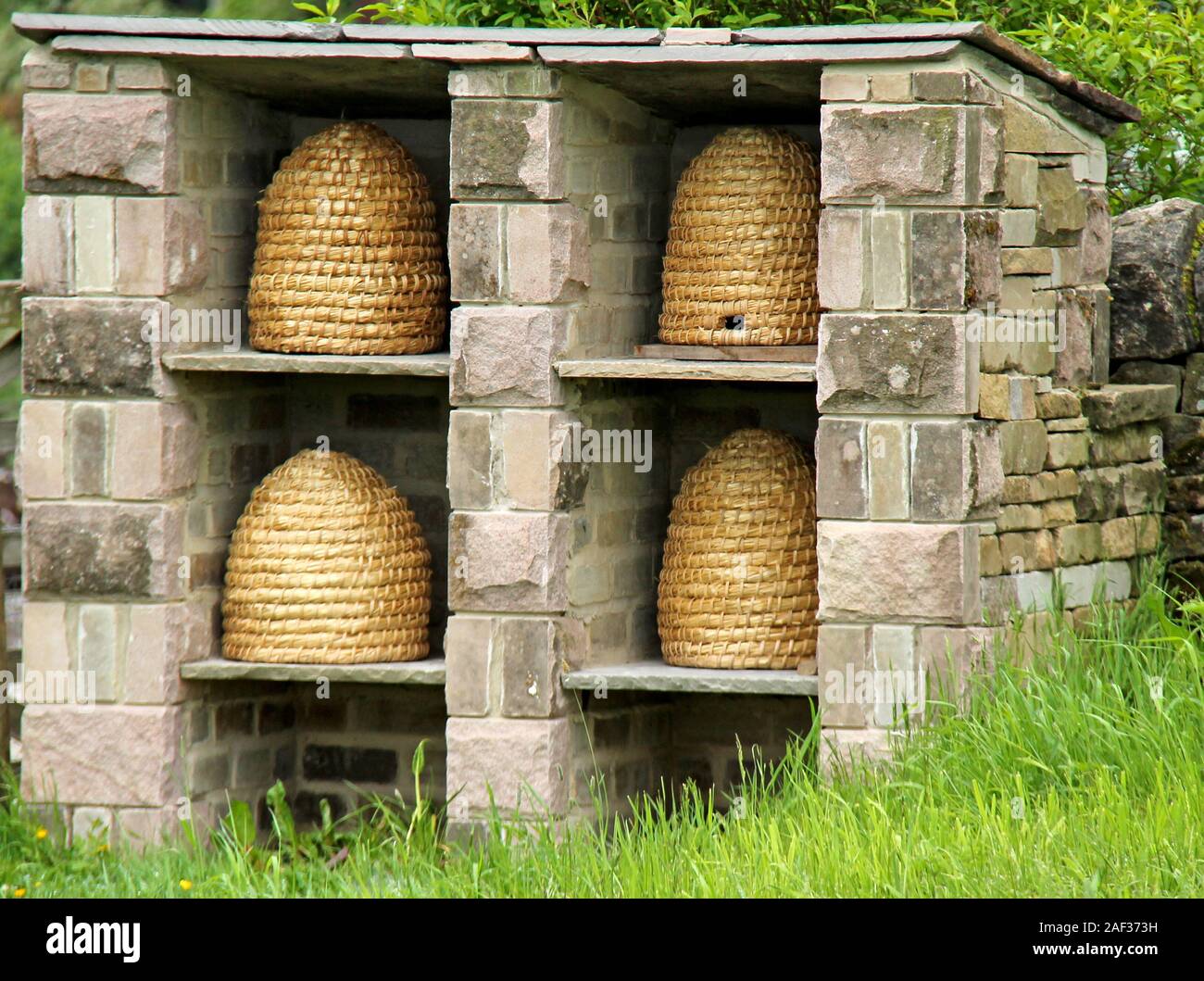 Quatre ruches en osier dans un abri de jardin en pierre. Banque D'Images