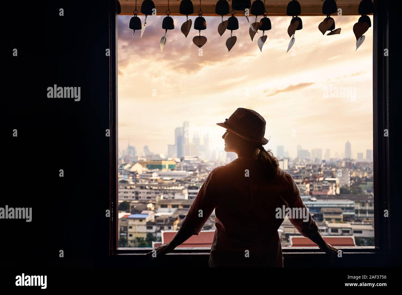 Silhouette of woman in hat est à la fenêtre de vue sur la ville de Bangkok de gratte-ciel du quartier des affaires à partir de la montagne d'or à la Pagode Wat Saket orange Banque D'Images