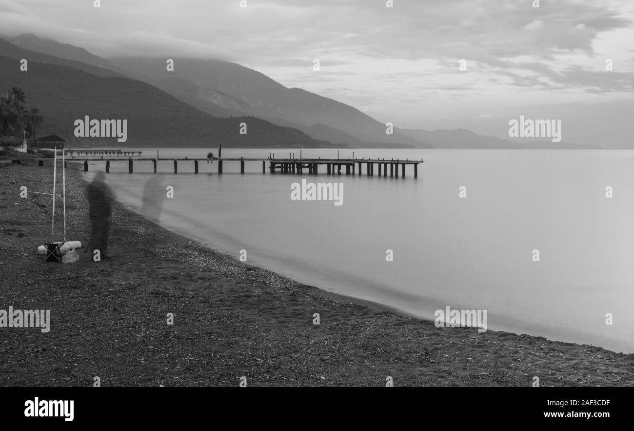 Noir et blanc en forme de plumes de l'image de la côte de la mer de rochers et vagues. Soft focus en raison d'une longue exposition. L'image artistique de pier et fisherman silhouet Banque D'Images