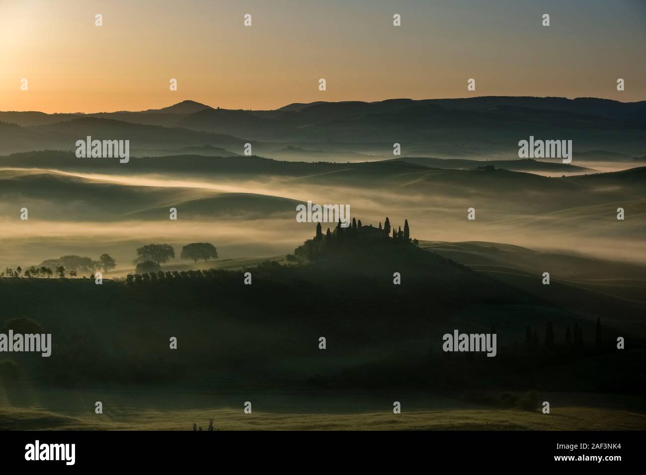 Vallonné typique campagne toscane, dans le Val d'Orcia, la ferme Podere Belvedere sur une petite colline et de brouillard dans les vallées, au lever du soleil Banque D'Images