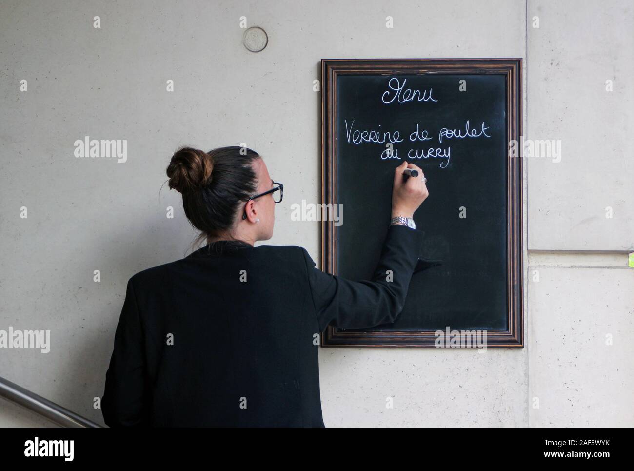 Jeune femme écrivant un menu de restaurant sur tableau noir sign in Paris, France Banque D'Images
