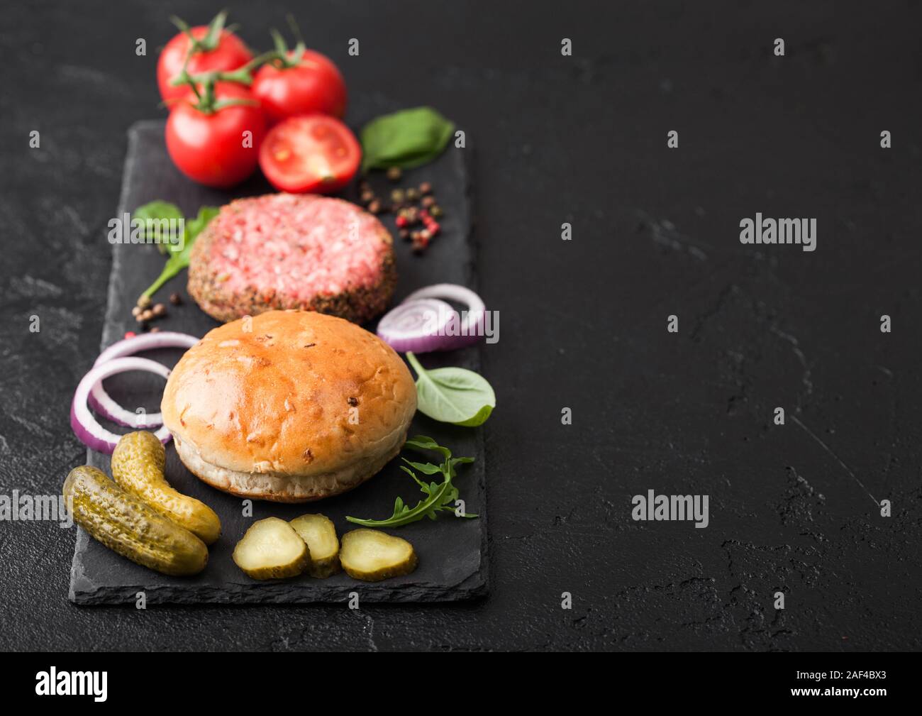 Les frais émincé de bœuf au poivre sur planche en pierre avec des oignons et des tomates, petits pains sur fond noir. Cornichons salés et de basilic. Vue d'en haut Banque D'Images