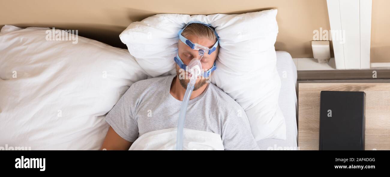 L'homme allongé sur le lit avec l'apnée du sommeil et l'appareil CPAP Banque D'Images