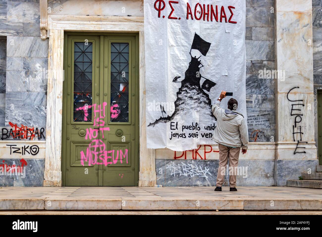 Un homme prenant des photos d'une bannière protet placé à l'entrée de l'Université polytechnique d'Athènes. Banque D'Images