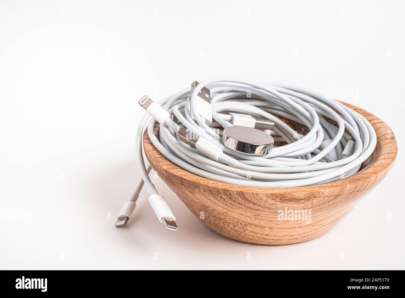 Plusieurs Apple blanc les câbles d'alimentation et les connecteurs en agitant un bol en bois fixés sur un fond blanc. Banque D'Images