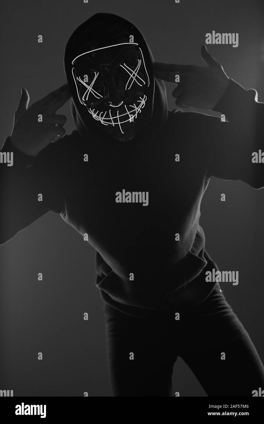 Portrait d'un homme anonyme dans un hoodie noir cachant son visage derrière un masque de néon effrayant. Studio shot. Banque D'Images