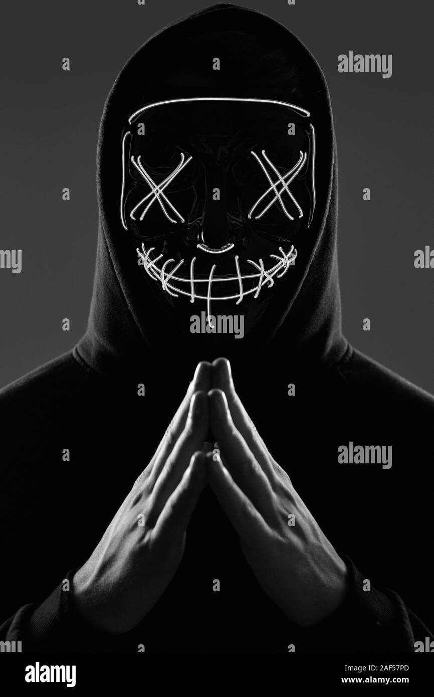 Portrait d'un homme anonyme dans un hoodie noir cachant son visage derrière un masque de néon effrayant. Studio shot. Banque D'Images