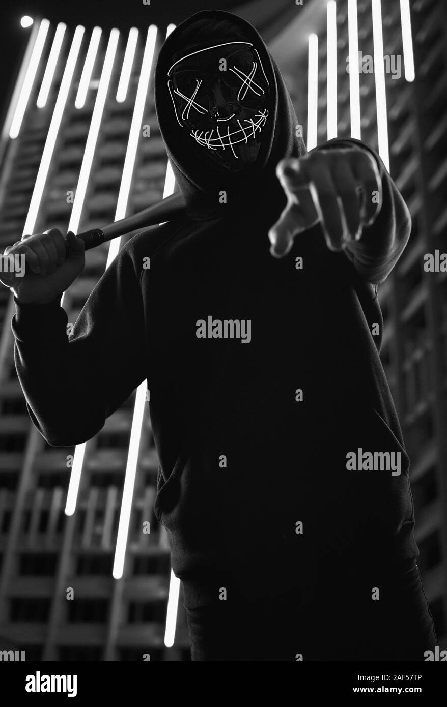 Portrait d'un criminel anonyme homme avec batte de baseball dans un hoodie noir cachant son visage derrière un masque de néon. Arrière-plan de ville lumineuse Banque D'Images