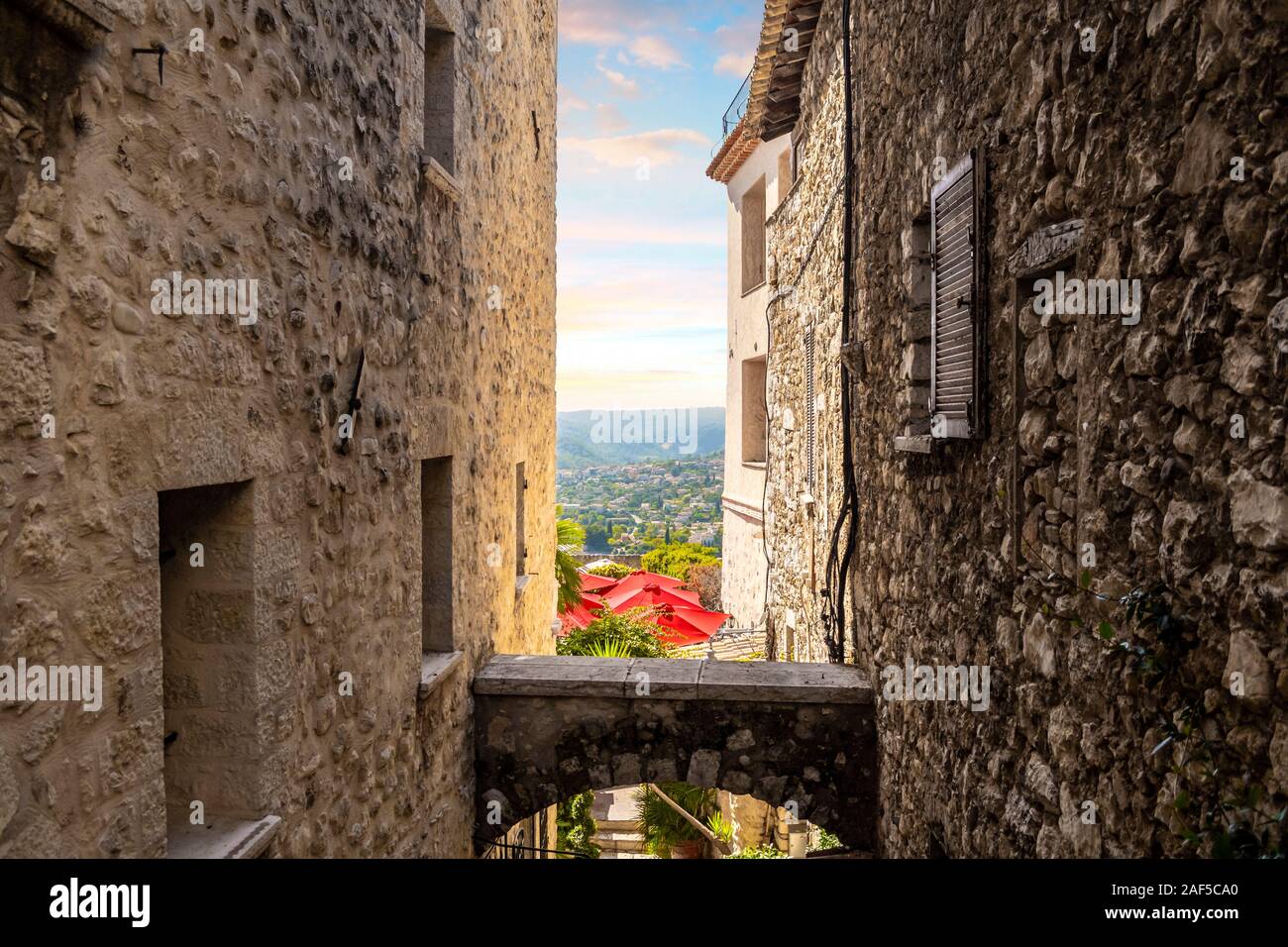 Les parapluies rouges d'un cafe patio et la campagne Alpes-Maritimes français sont visibles d'une ruelle dans la ville médiévale de Saint Paul de Vence, France Banque D'Images