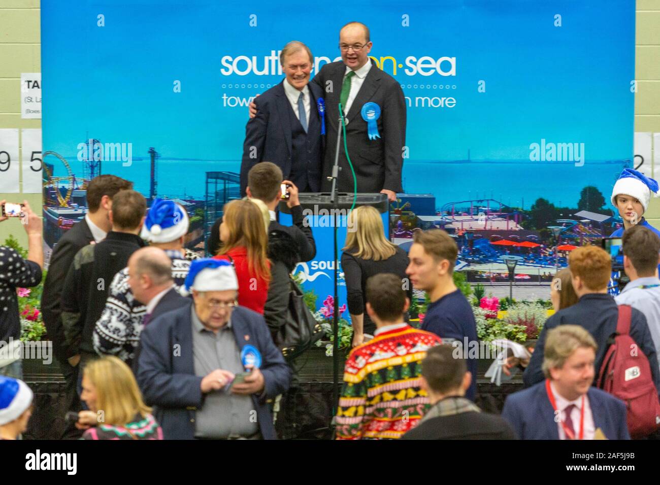 Southend on Sea, Royaume-Uni. 13 décembre 2019. Les candidats du Parti conservateur David Amess et James Duddridge célèbrent les résultats respectifs des élections sur scène à Southend-on-Sea, Essex. L'événement présente des tenues festives parmi les participants, y compris des vêtements sur le thème de Noël et des chapeaux de Père Noël bleus. Une grande bannière indiquant « southend-on-Sea Town centre & more » est visible en arrière-plan, indiquant l’emplacement. Penelope Barritt/Alamy Live News Banque D'Images