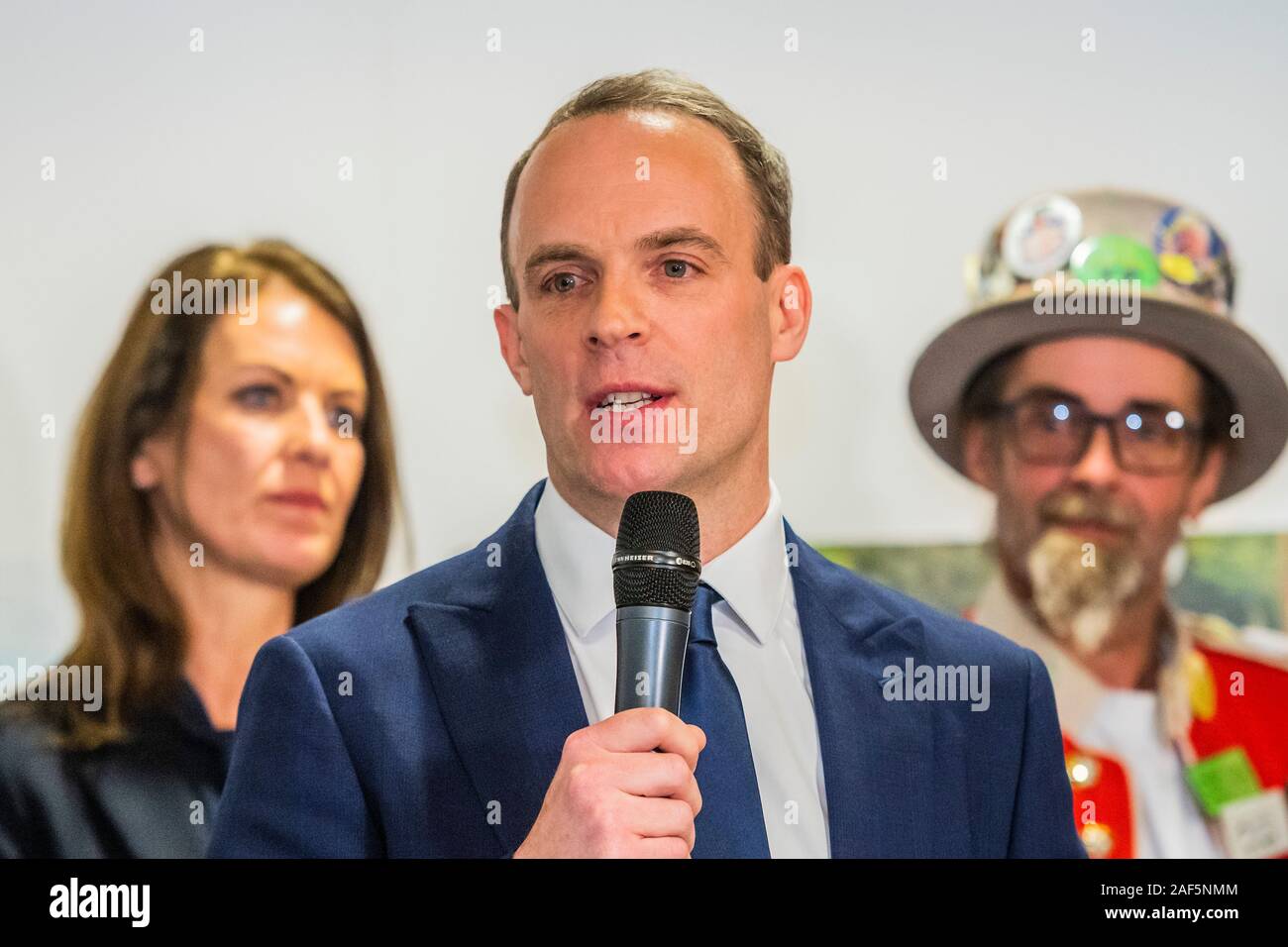 Esher, Londres, Royaume-Uni. 13 Décembre, 2019. Dominic Raab fait son discours d'acceptation après l'winsning par 31 132 voix contre 28389 pour Monica Harding (photo derrière avec le Baron de blaireau le Monster Raving Loony partie) - Le résultat à l'Esher et Walton dans la circonscription 2019 Élection générale. Où Dominic Raab est le député conservateur sortant et est poursuivi par Monica Harding, de la lib Dems. Crédit : Guy Bell/Alamy Live News Banque D'Images