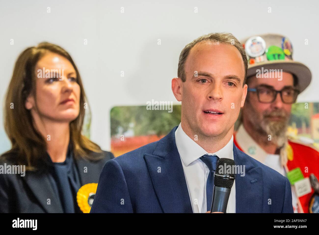 Esher, Londres, Royaume-Uni. 13 Décembre, 2019. Dominic Raab fait son discours d'acceptation après l'winsning par 31 132 voix contre 28389 pour Monica Harding (photo derrière avec le Baron de blaireau le Monster Raving Loony partie) - Le résultat à l'Esher et Walton dans la circonscription 2019 Élection générale. Où Dominic Raab est le député conservateur sortant et est poursuivi par Monica Harding, de la lib Dems. Crédit : Guy Bell/Alamy Live News Banque D'Images