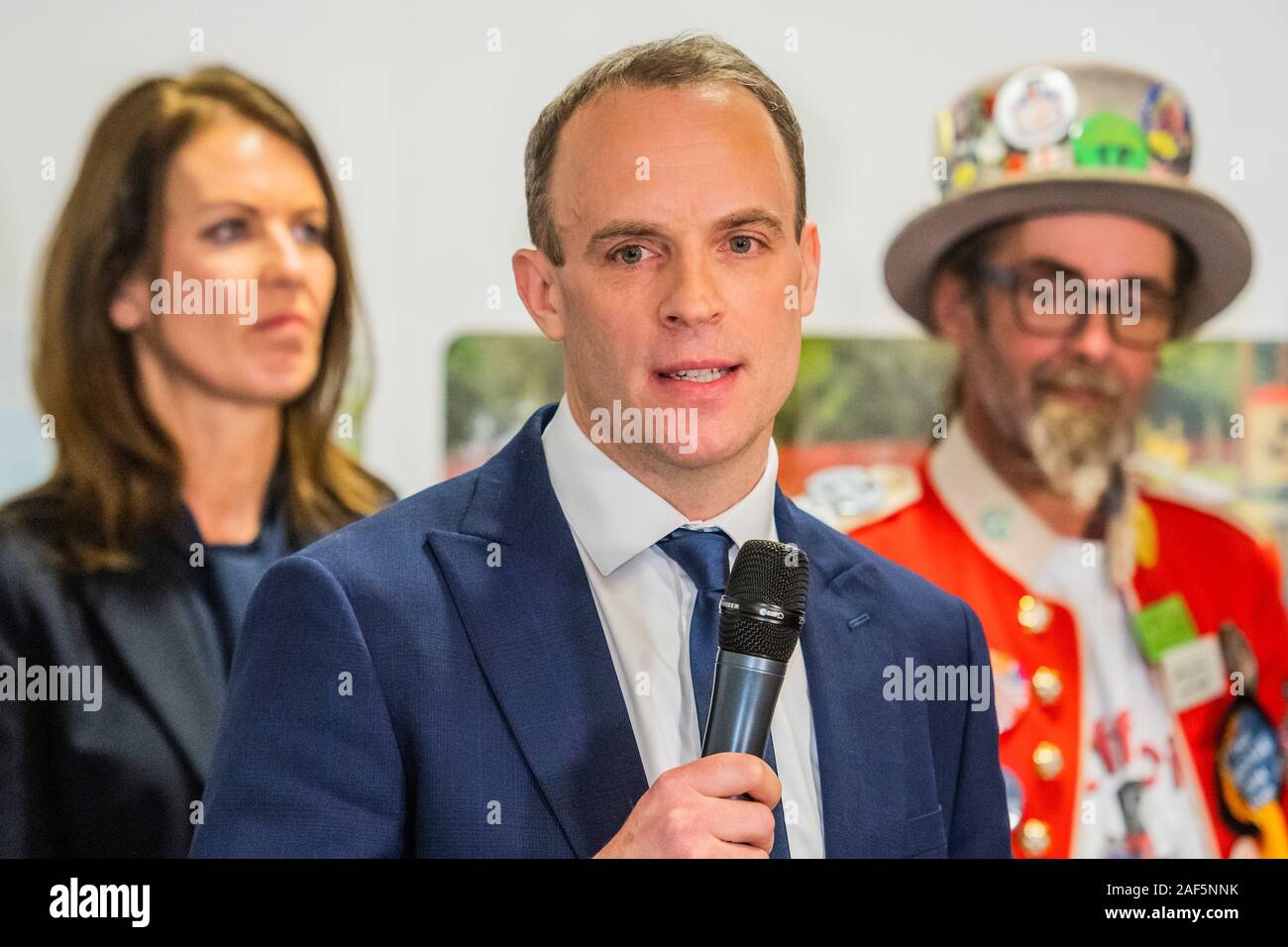 Esher, Londres, Royaume-Uni. 13 Décembre, 2019. Dominic Raab fait son discours d'acceptation après l'winsning par 31 132 voix contre 28389 pour Monica Harding (photo derrière avec le Baron de blaireau le Monster Raving Loony partie) - Le résultat à l'Esher et Walton dans la circonscription 2019 Élection générale. Où Dominic Raab est le député conservateur sortant et est poursuivi par Monica Harding, de la lib Dems. Crédit : Guy Bell/Alamy Live News Banque D'Images