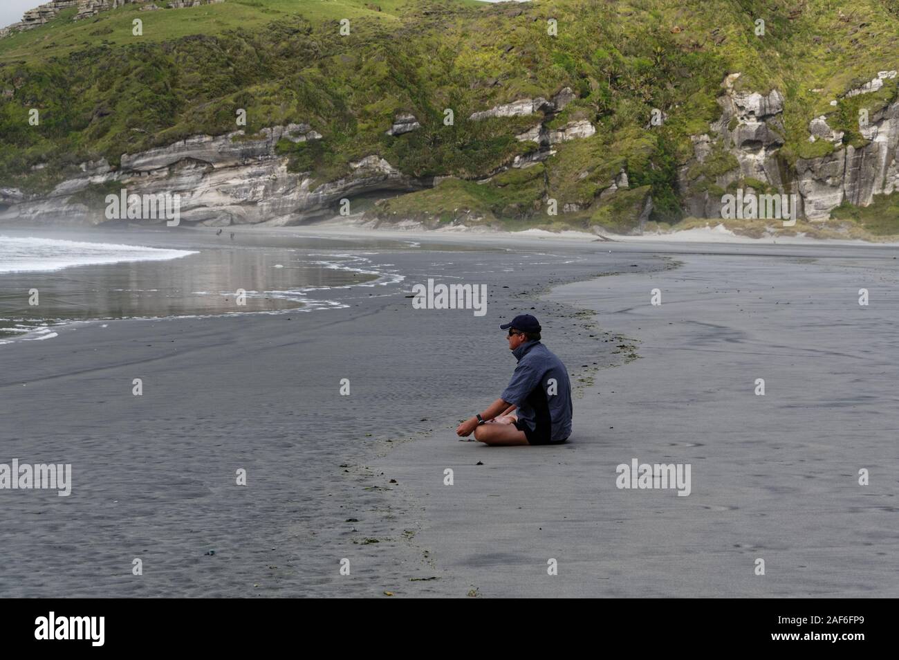 Un homme est assis jambes croisées sur la plage que les vagues genoux vers lui Banque D'Images