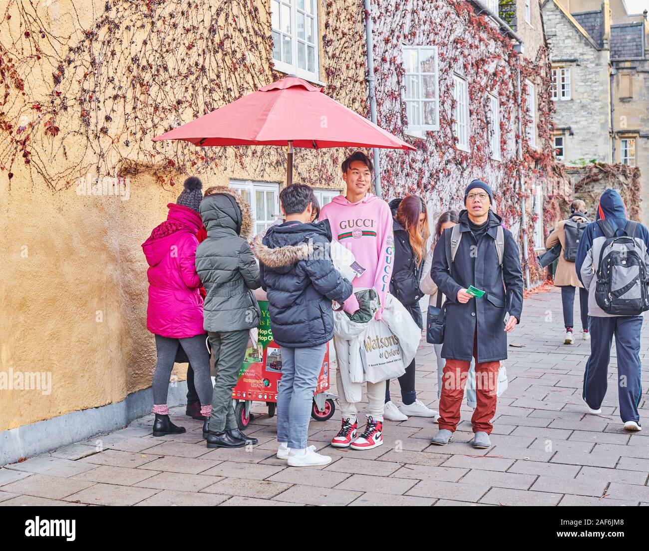 Un groupe de touristes chinois attendre le hop-on, hop-bus de l'extérieur de Trinity College, Université d'Oxford, en Angleterre, sur une froide journée d'hiver. Banque D'Images