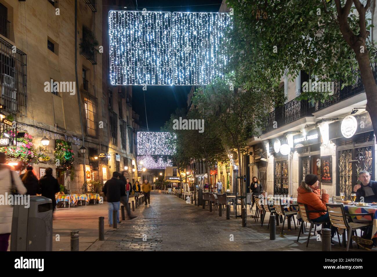 Les gens assis dehors sur des tables à Cava de San Miguel à Madrid, Espagne. C'est décembre proche de Noël et décorations ornent les rues. Banque D'Images