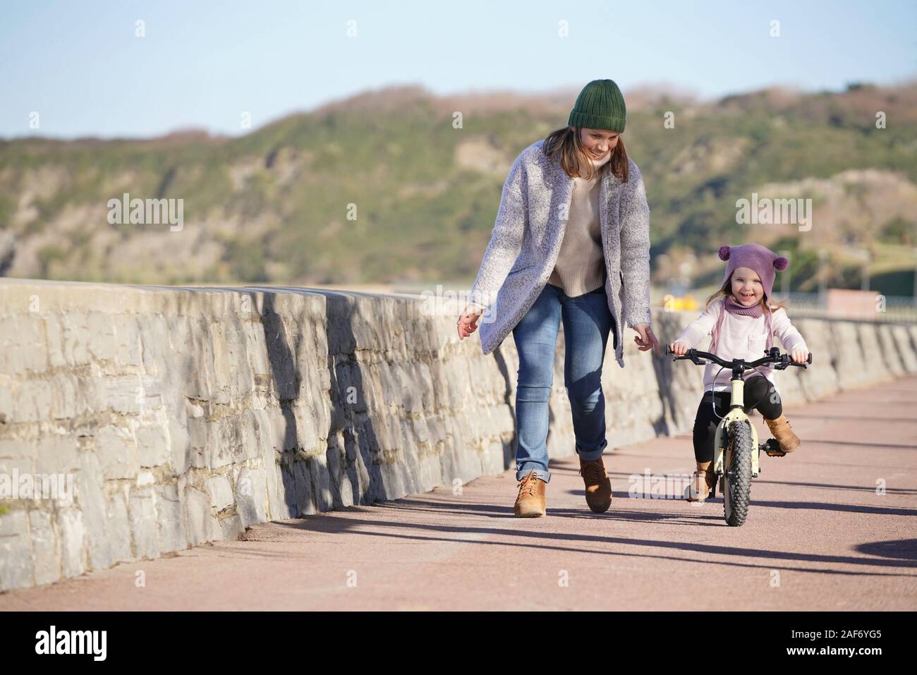 Mère d'exécution à côté de jeune fille équitation vélo Banque D'Images