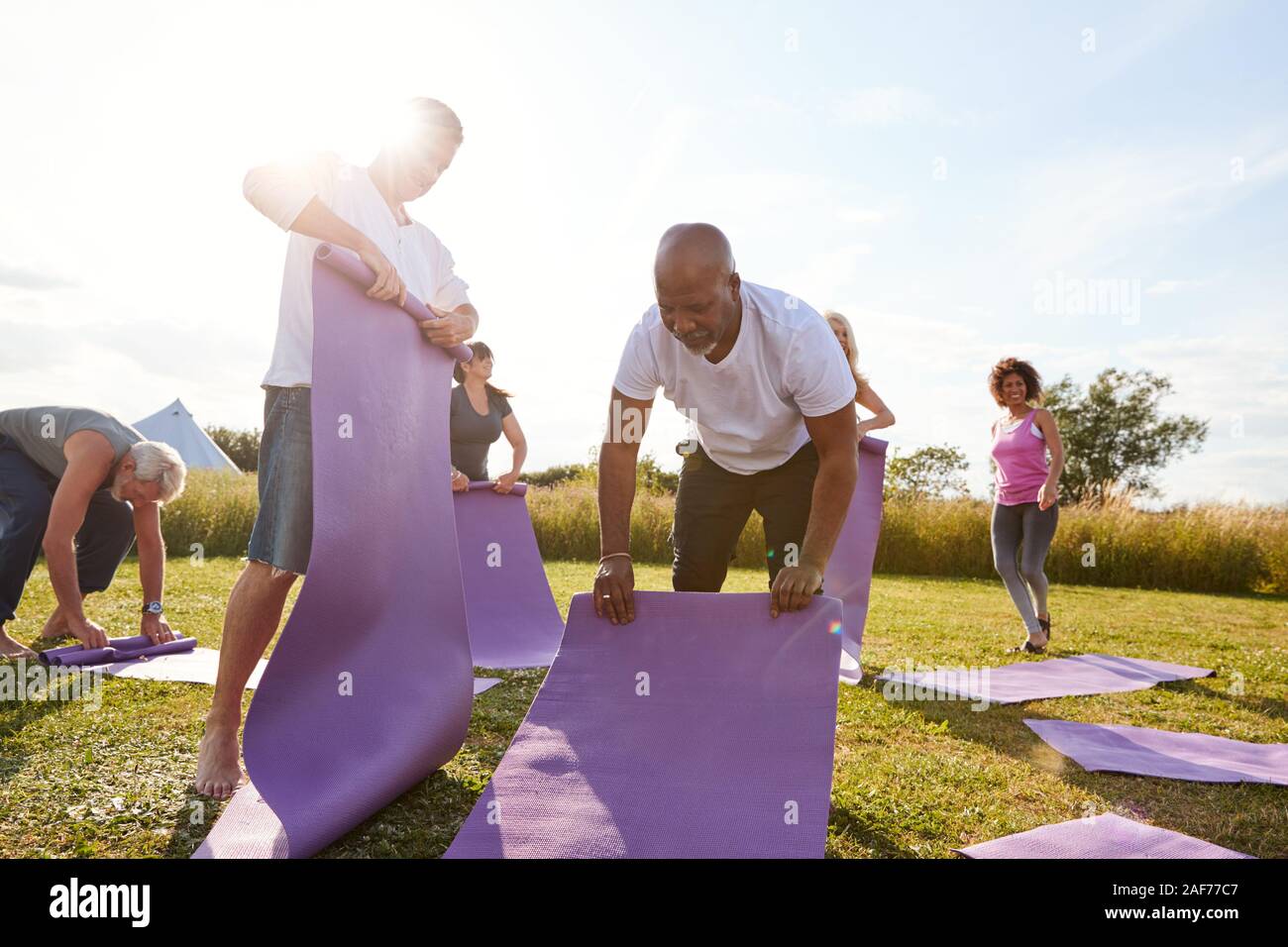 Groupe d'âge Hommes et femmes Rouler de tapis d'exercice à la fin de la classe de yoga en plein air Banque D'Images