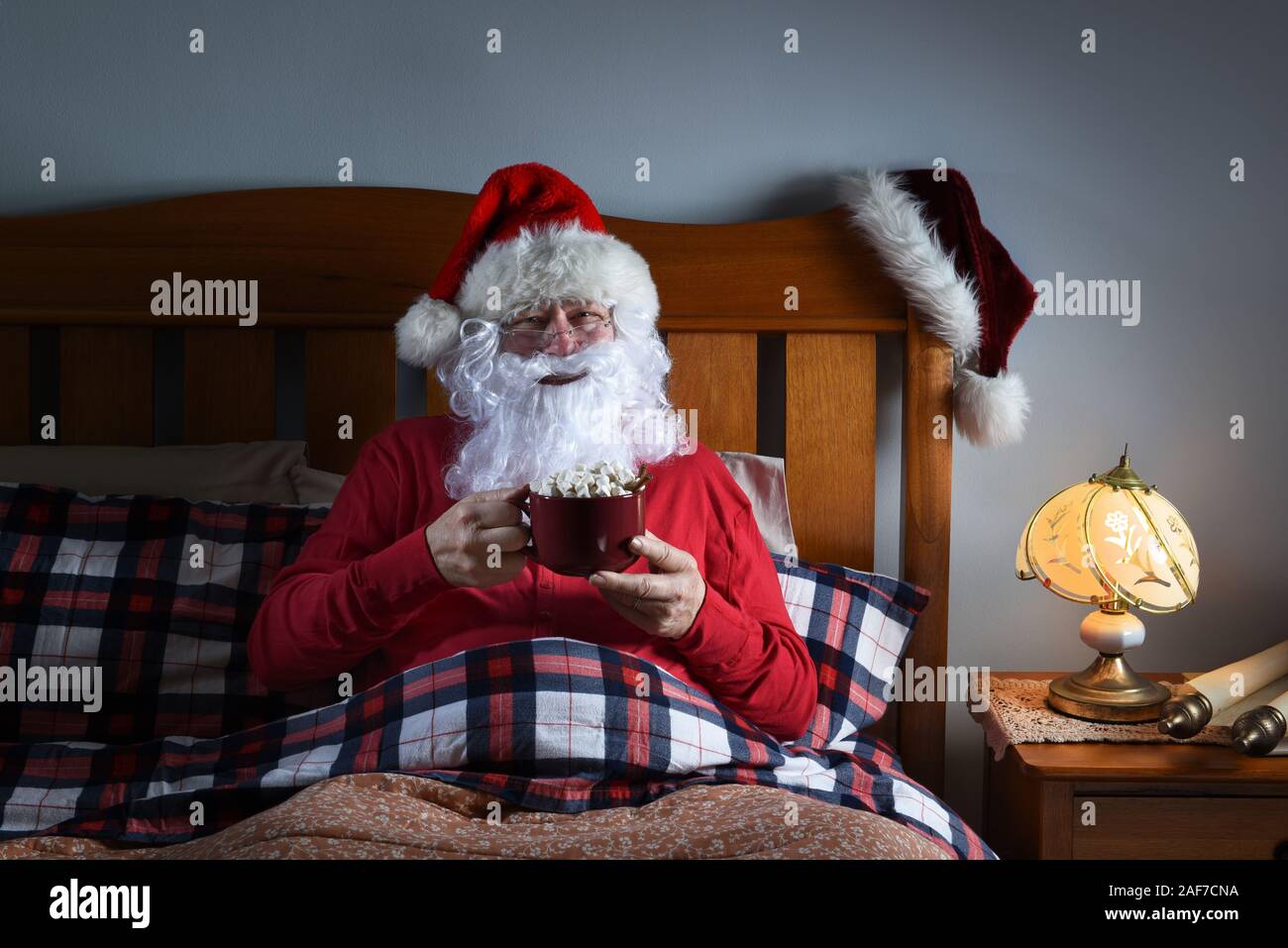 Père Noël assis dans le lit avec une grande tasse de chocolat chaud avant qu'il va dormir la veille de Noël. Banque D'Images