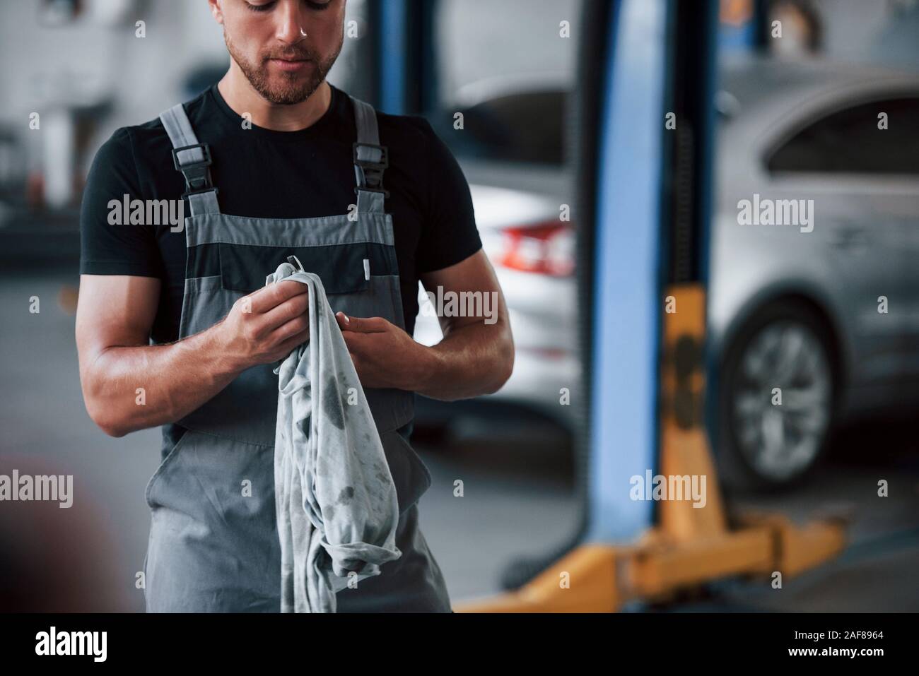 Journée ordinaire au travail. L'homme en chemise noire et grise est uniforme dans le garage après la réparation de voiture cassée Banque D'Images