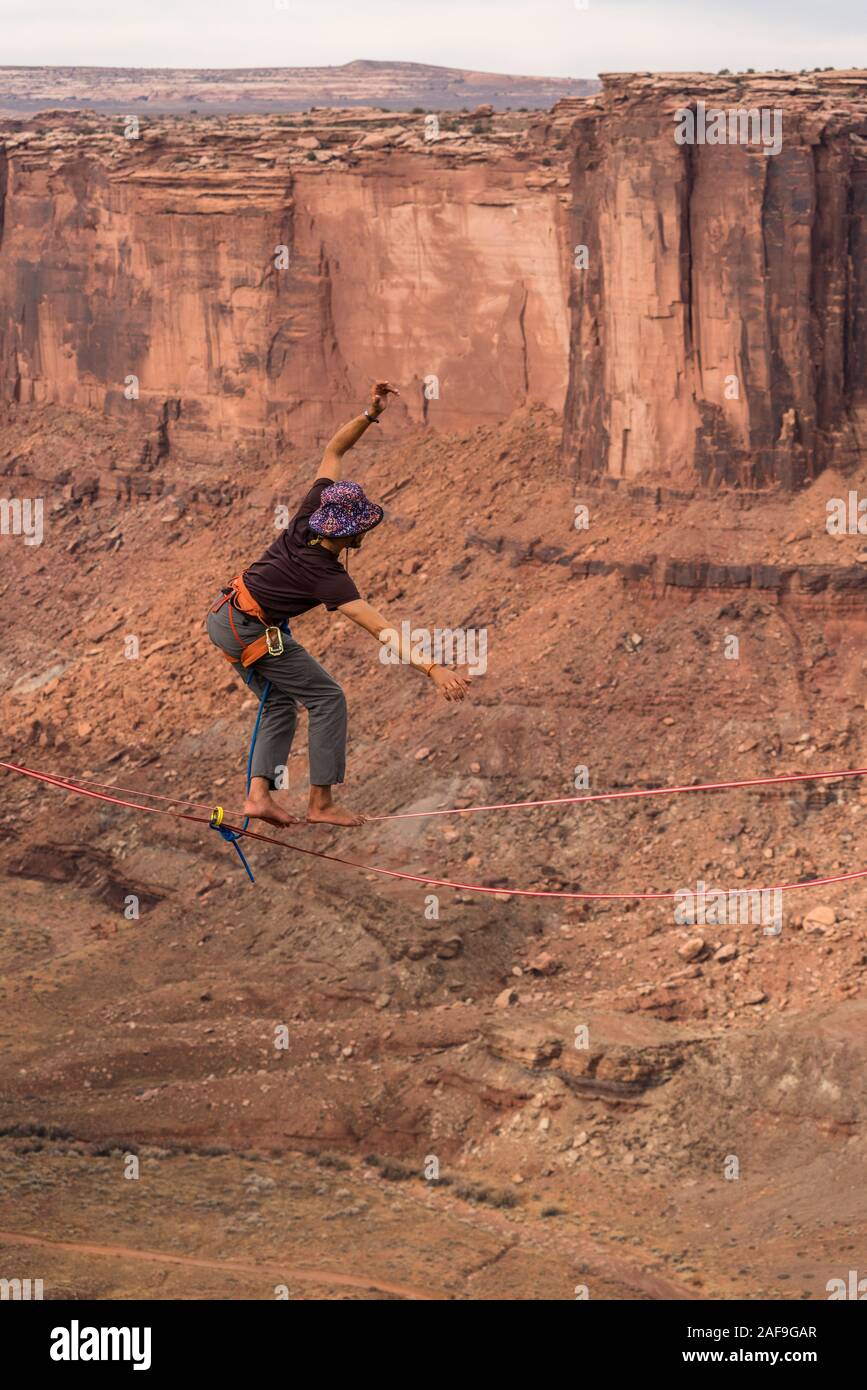 Un jeune homme slackline ou highlining lutte pour maintenir l'équilibre des centaines de pieds au-dessus du Canyon de minéraux près de Moab, en Utah pendant un rassemblement highline. Banque D'Images