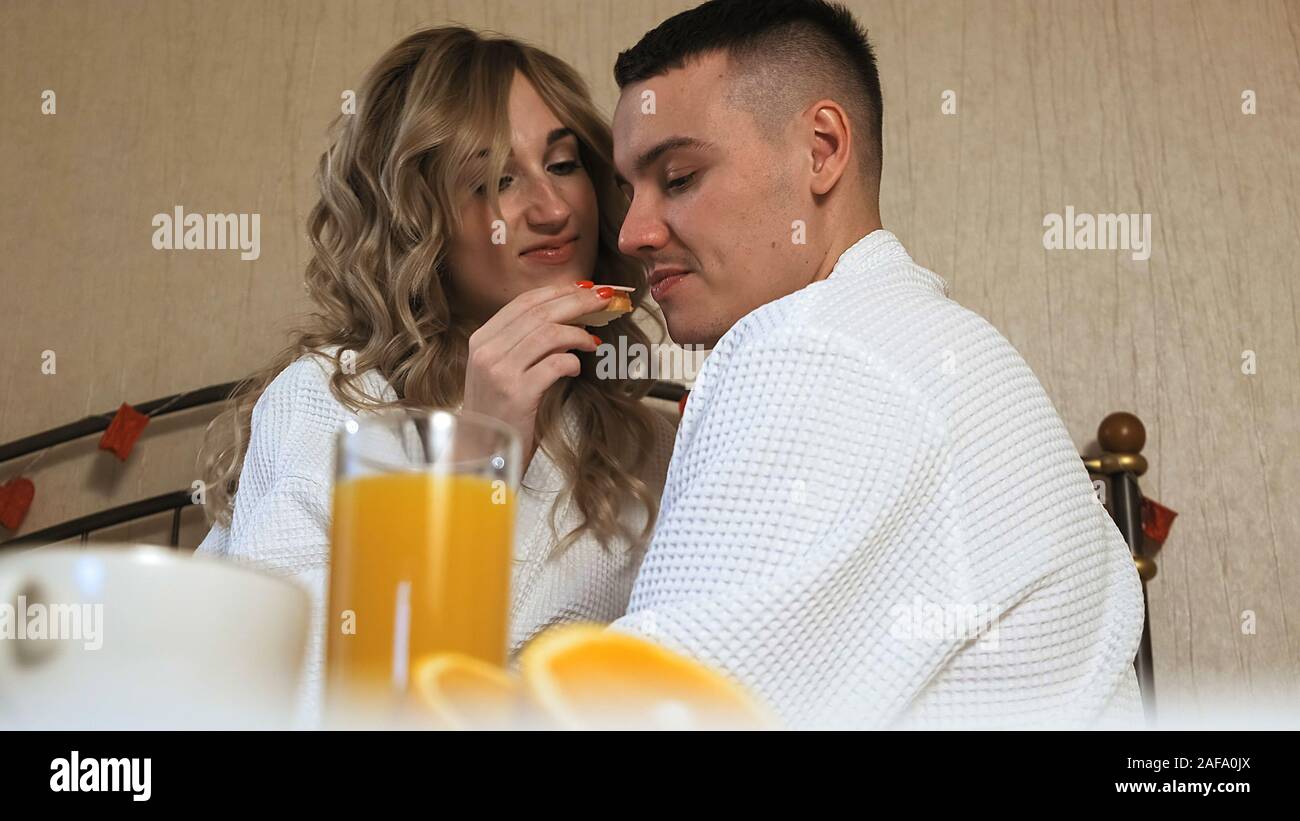 Jeune couple romantique amoureux le petit déjeuner au lit. Jolie petite amie nourrit son petit ami un délicieux sandwich Banque D'Images