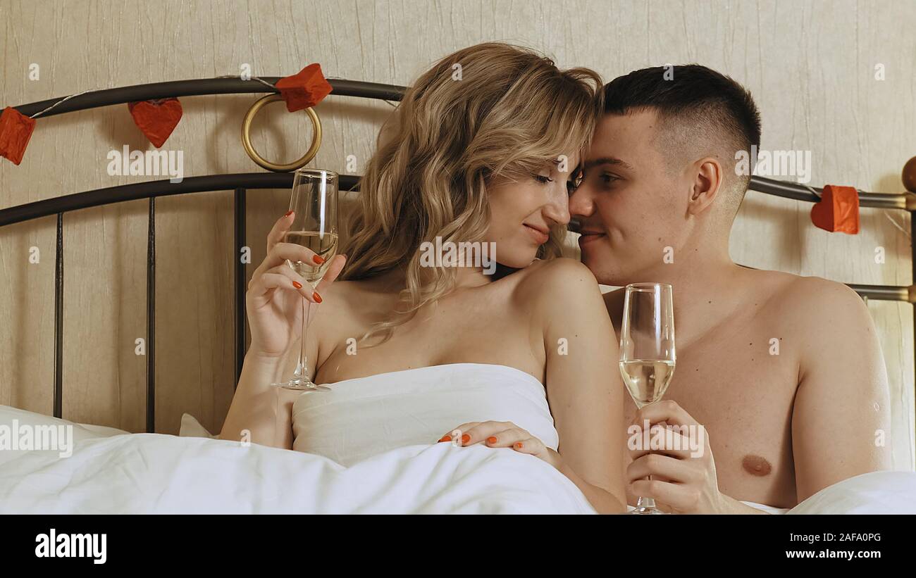 Un jeune couple est assis dans le lit, sous une couverture. Ils boivent du champagne et profiter de l'autre. Date romantique dans une chambre d'hôtel Banque D'Images