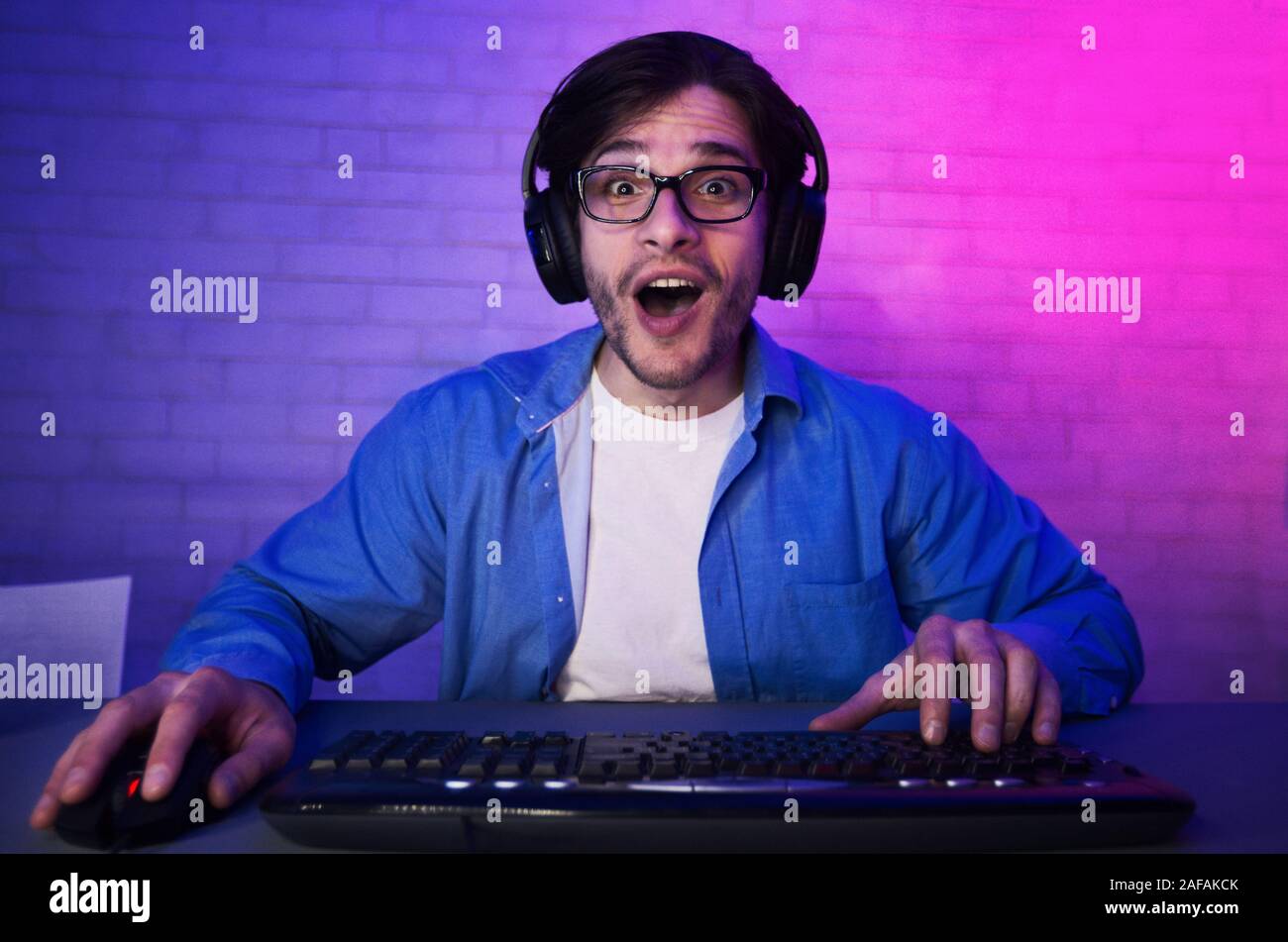L'homme surpris à jouer en ligne jeu d'ordinateur, wearing headset Banque D'Images