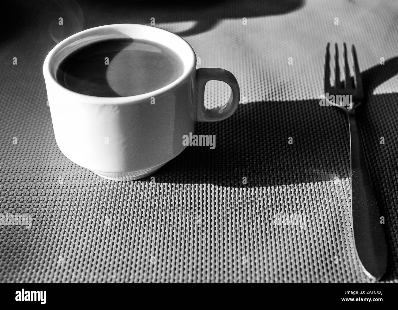 Profondeur de champ (selective focus) image avec une tasse de café chaud et d'une fourchette sur une table pendant le petit déjeuner tôt le matin. Le noir et blanc Banque D'Images