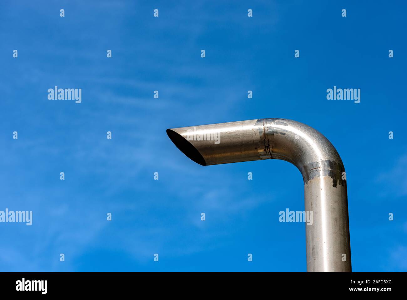 Close-up d'un tuyau d'échappement en acier sur un fond bleu ciel clair avec des nuages Banque D'Images