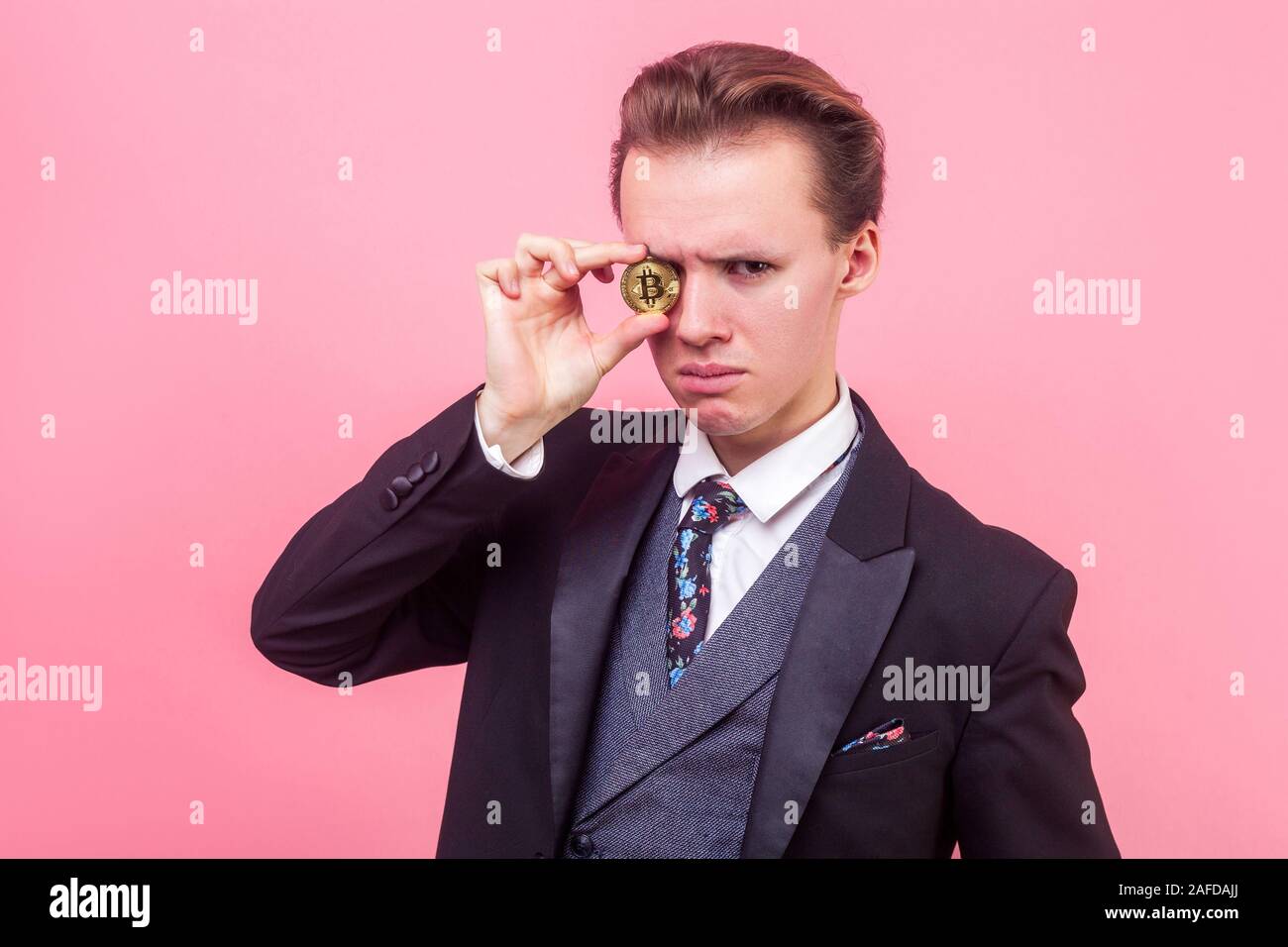 Portrait de l'homme malheureux en costume élégant et élégant avec coupe de cheveux couvrant les yeux à bitcoin or, looking at camera avec mécontentement expressi Banque D'Images