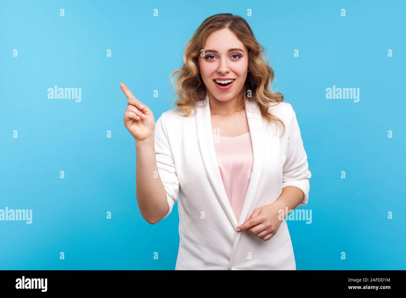 Portrait de femme intelligente se demande avec les cheveux ondulés en veste blanche montre de l'index et à la surprise, bonne idée de faire signer, si créatif soudaine Banque D'Images