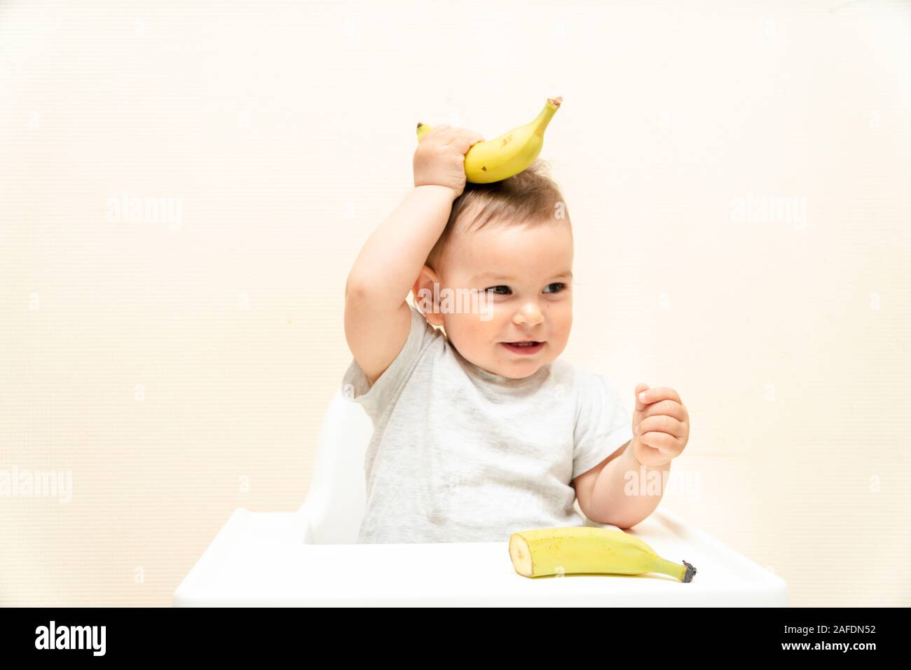 Funny little toddler eating banana sur une chaise haute bébé l'alimentation de l'espace de copie Banque D'Images