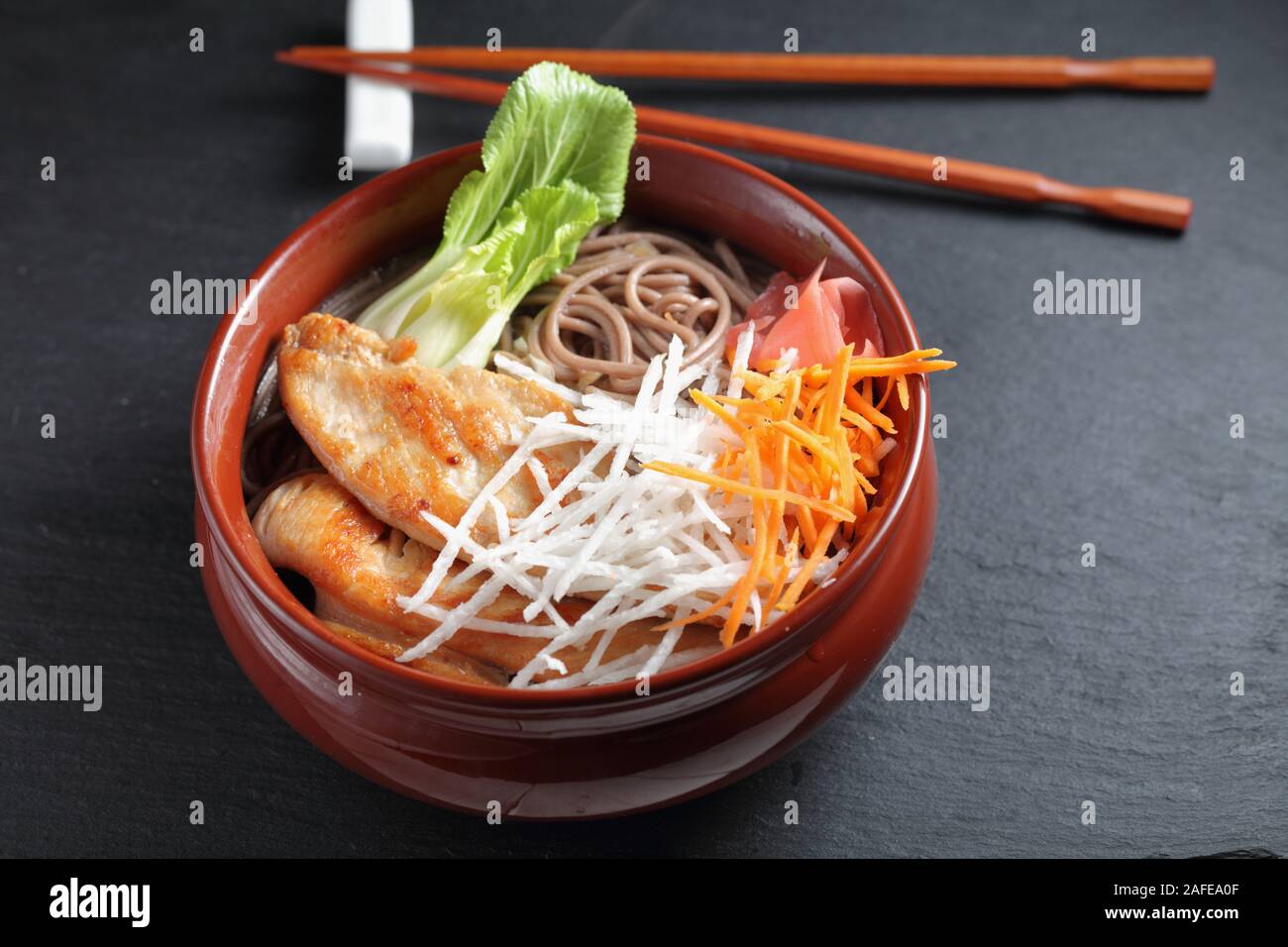 Partie de la soupe aux nouilles soba avec des tranches de poulet frit, du radis daikon, carotte, gingembre mariné, et feuilles de bok choy Banque D'Images