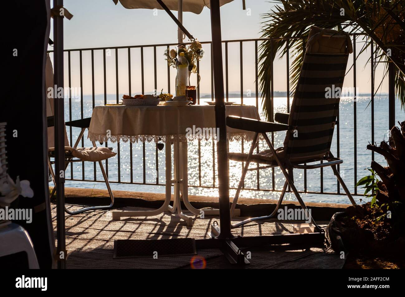 Petit-déjeuner servi une table pour deux avec deux chaises et parasol voyage derrière les balustrades métalliques sur la plage du lac de Garde à la fin de l'aube. La Lombardie, ita Banque D'Images