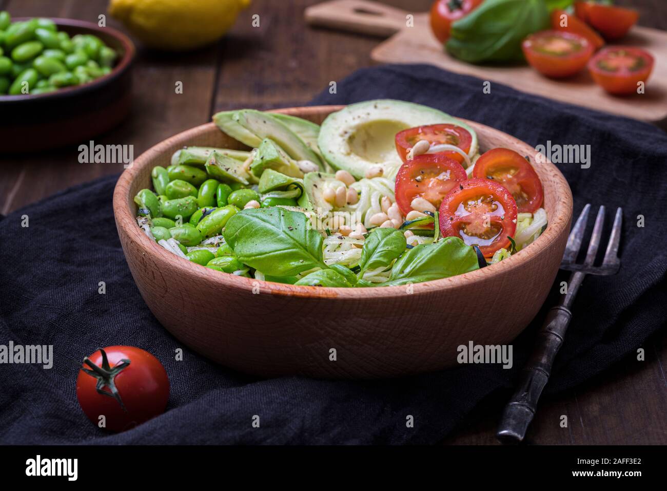 Vue latérale d'une salade fraîche, saine avec zoodles nouilles aux courgettes, tomates, avocat et bébé edamame beans. La salade n'est dans un bol en bois sur une b Banque D'Images