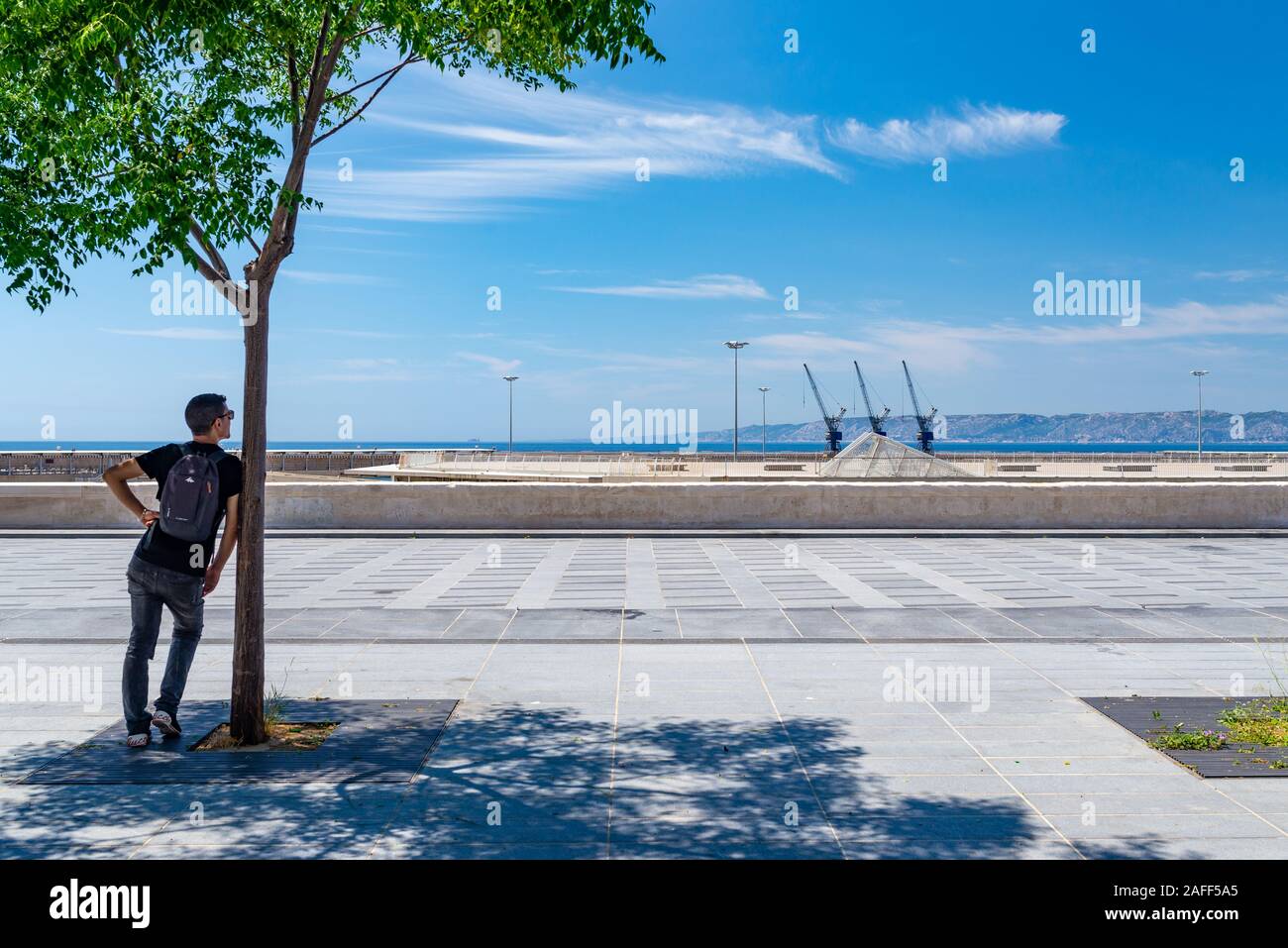 Un homme méconnaissable, vu de derrière, à la recherche dans le port d'une place publique, prises sur un après-midi ensoleillé du début de l'été, Marseille, France Banque D'Images