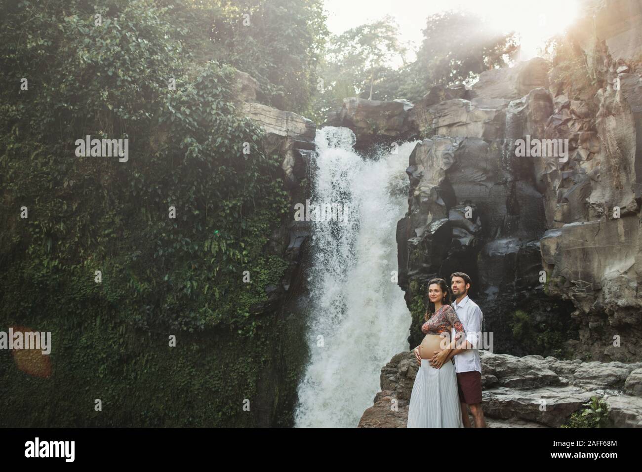 L'Accouchement à Bali. Les jeunes femmes enceintes de voyage couple sur Tegenungan cascade. Les valeurs d'harmonie familiale. Heureux ensemble, la grossesse billet de vie. Beau matin nature. Concept de la maternité. Banque D'Images