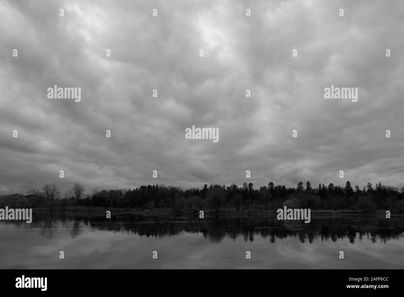 Tourné en noir et blanc de l'épaisse couverture nuageuse et arbres se reflétant dans un lac - le lac Dow, Ottawa, Ontario, Canada. Banque D'Images