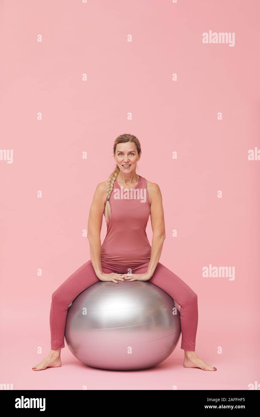 Portrait de femme mature moderne faire du sport avec des exercices de fitness ball contre fond rose pastel, copy space Banque D'Images