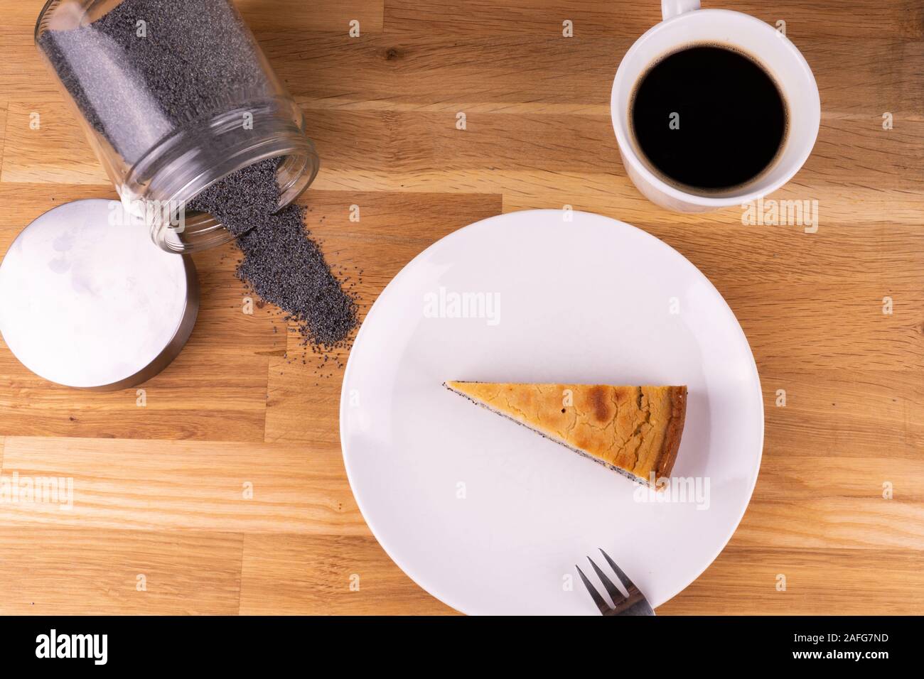 Un morceau de gâteau au fromage vegan aux graines de pavot avec une fourchette, une tasse de café et les graines de pavot sur une table en bois - télévision lay Banque D'Images