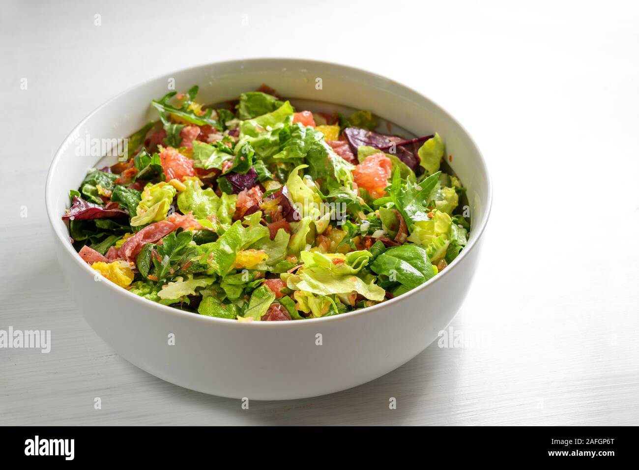 Salade de laitue en bonne santé, orange, pamplemousse, salami et les pignons de pin dans un grand bol, gris à fond blanc avec copie espace, accent sélectionné, na Banque D'Images