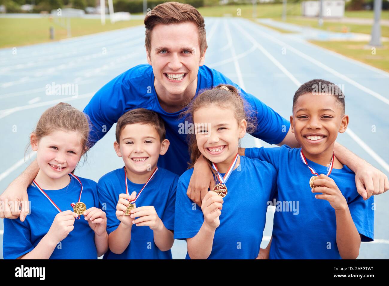Portrait des enfants avec entraîneur masculin montrant outre de gagnants de médailles sur la Journée des sports Banque D'Images