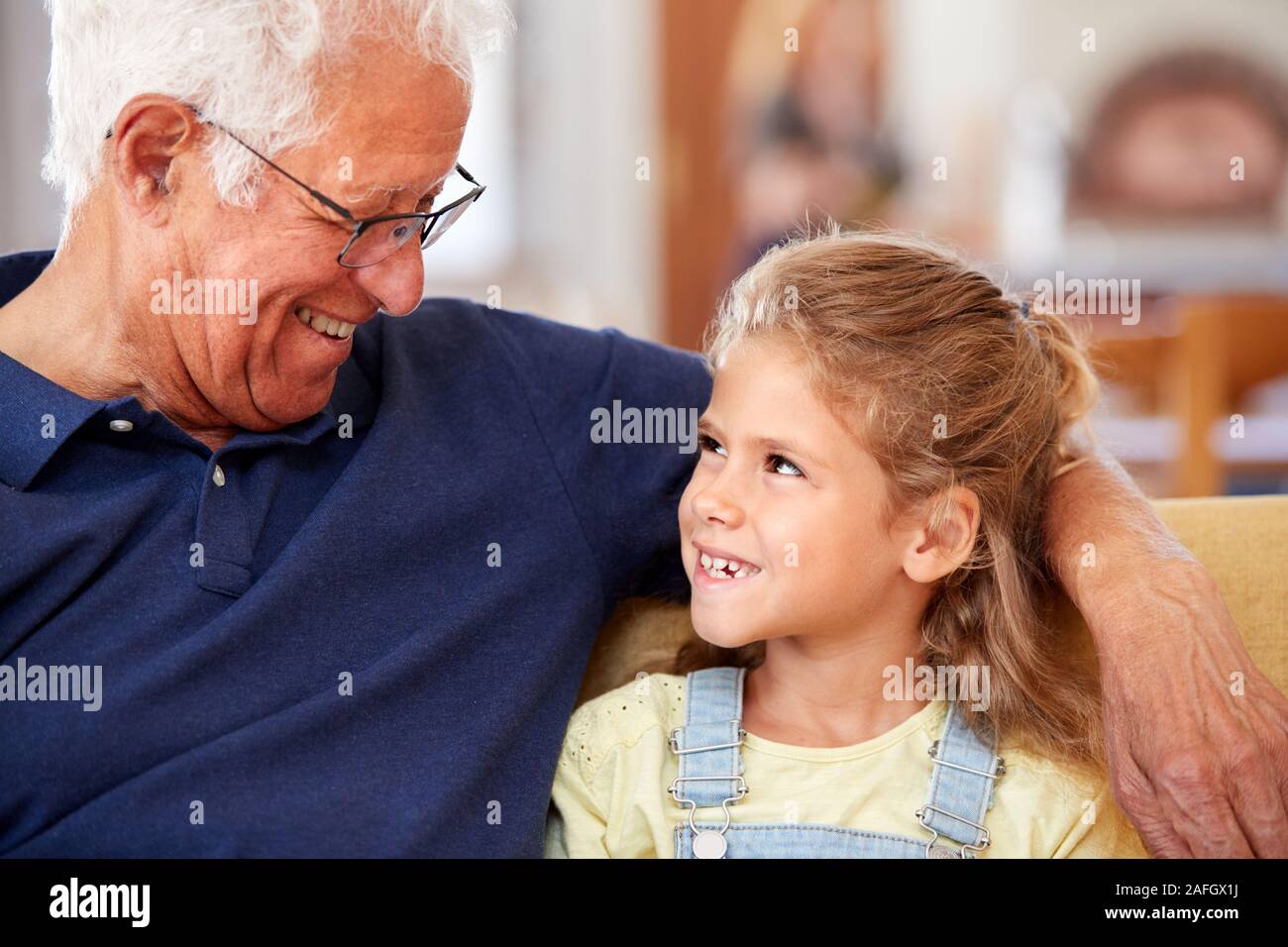 Grand-père avec sa petite-fille souriant assis sur le canapé à la maison Banque D'Images